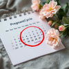 Calendar with menstrual days, pregnancy test, and flowers.