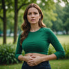 Woman holding stomach, looking uncomfortable, green background.