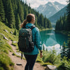 Woman hiking on a mountain trail with a backpack, lake and forest in the background, enjoying an outdoor adventure.