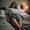 Woman peacefully sleeping on her side in period shorts, wrapped in a cozy blanket, in a serene bedroom.